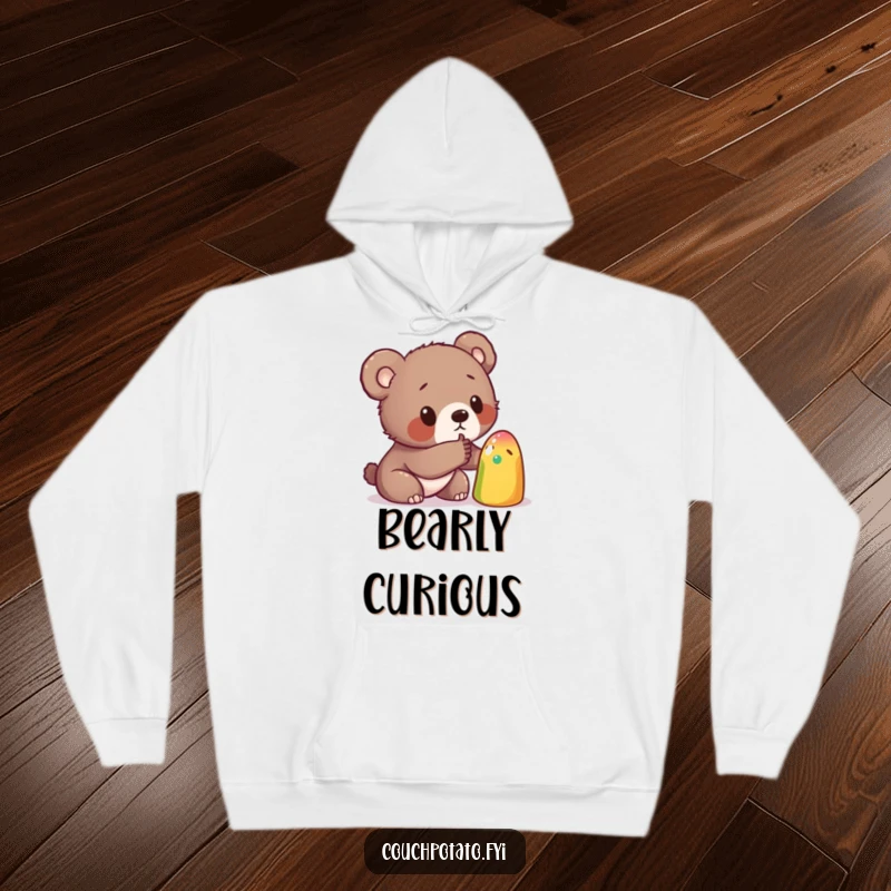 Funny hoodie depicting a curious bear cub gently poking a strange, colorful object, perfect for cozy moments of imagined exploration.